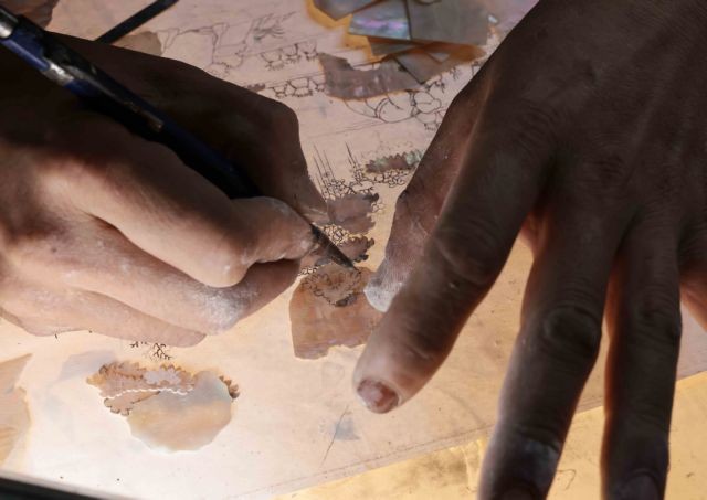 An artisan sketching designs onto mother-of-pearl and shell.